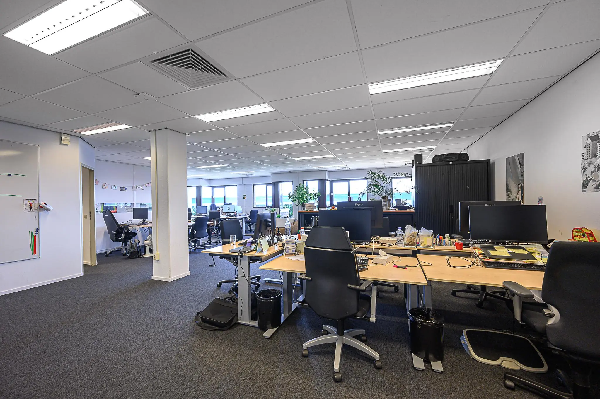 Moderne open kantoorruimte met meerdere bureaus, computerschermen en bureaustoelen bij daglicht.